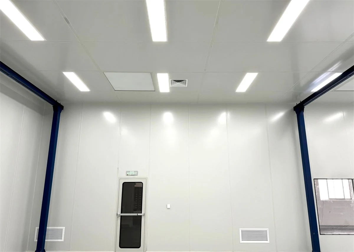 Bright pharmaceutical cleanroom interior with smooth white sandwich wall panels, flush ceiling lighting and an emergency exit door