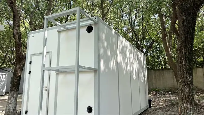 Three-quarter view of the ark-style modular laboratory showing the insulated white panel shell and external service frame among trees